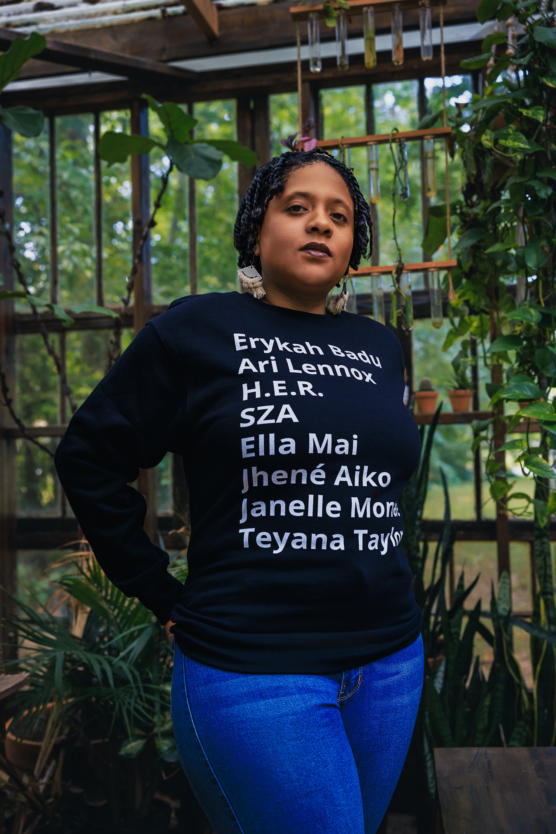 woman wearing - Sweater with minimalist typography listing female R&B singers: Erykah Badu, Ari Lennox, H.E.R., SZA, Ella Mai, Jhene Aiko, Janelle Monae, and Teyana Taylor.