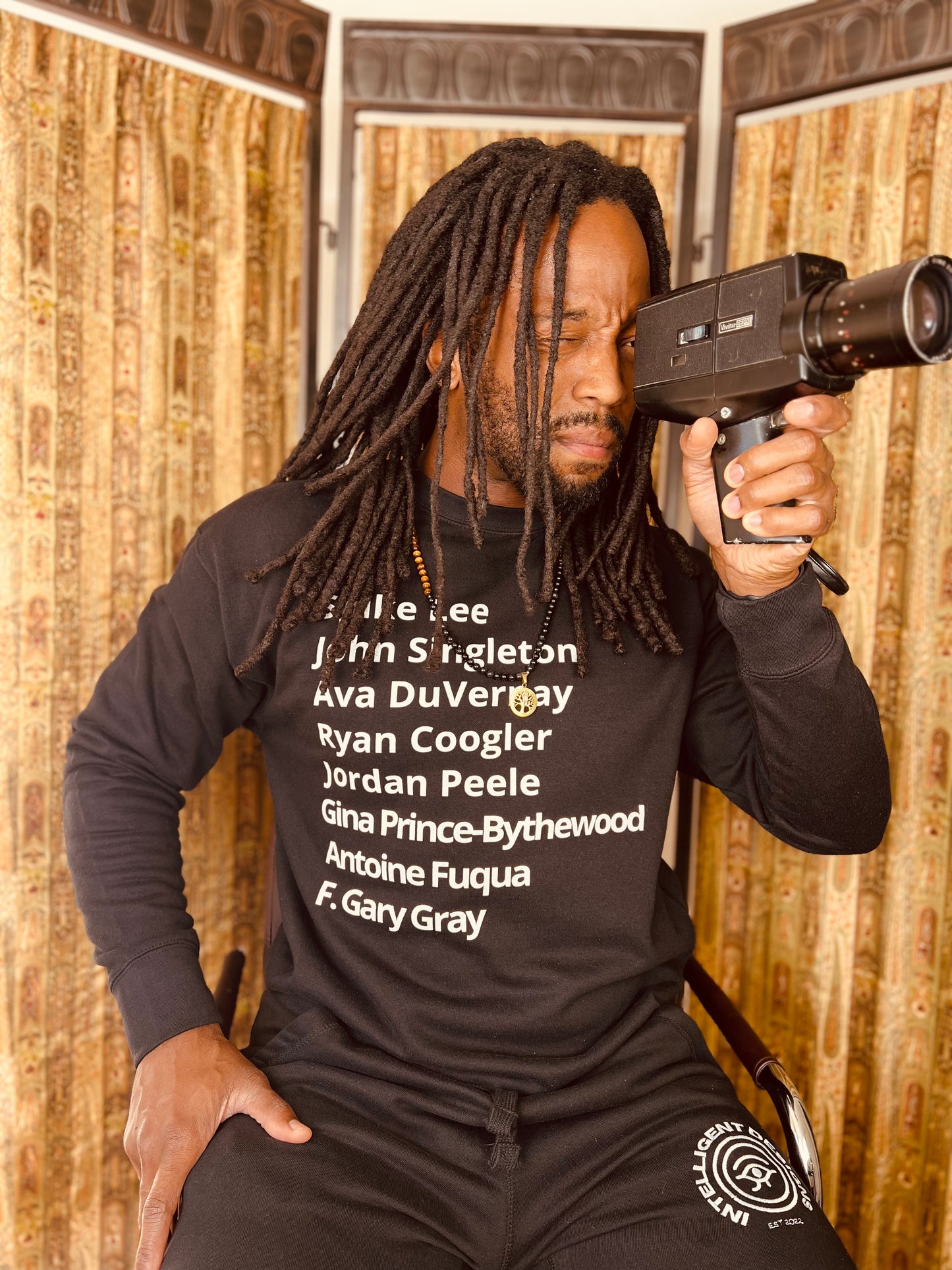 man wearing crew neck sweater with minimalist typography listing black filmmakers and cinema directors: Spike Lee, John Singleton, Ava DuVernay, Ryan Coogler, Jordan Peele, Gina Prince-Bythewood, Antoine Fuqua, F. Gary Gray